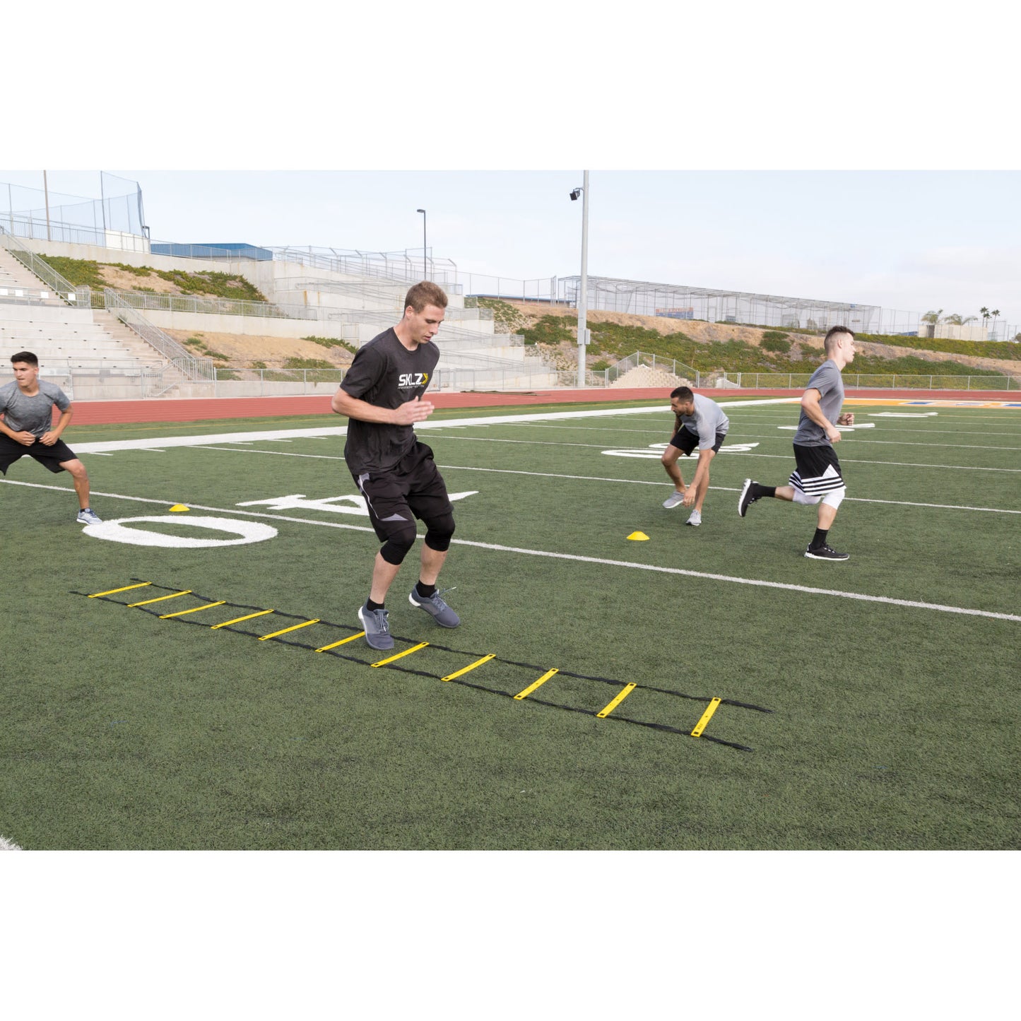 Athletes perform agility drills on a football field during training session outdoors