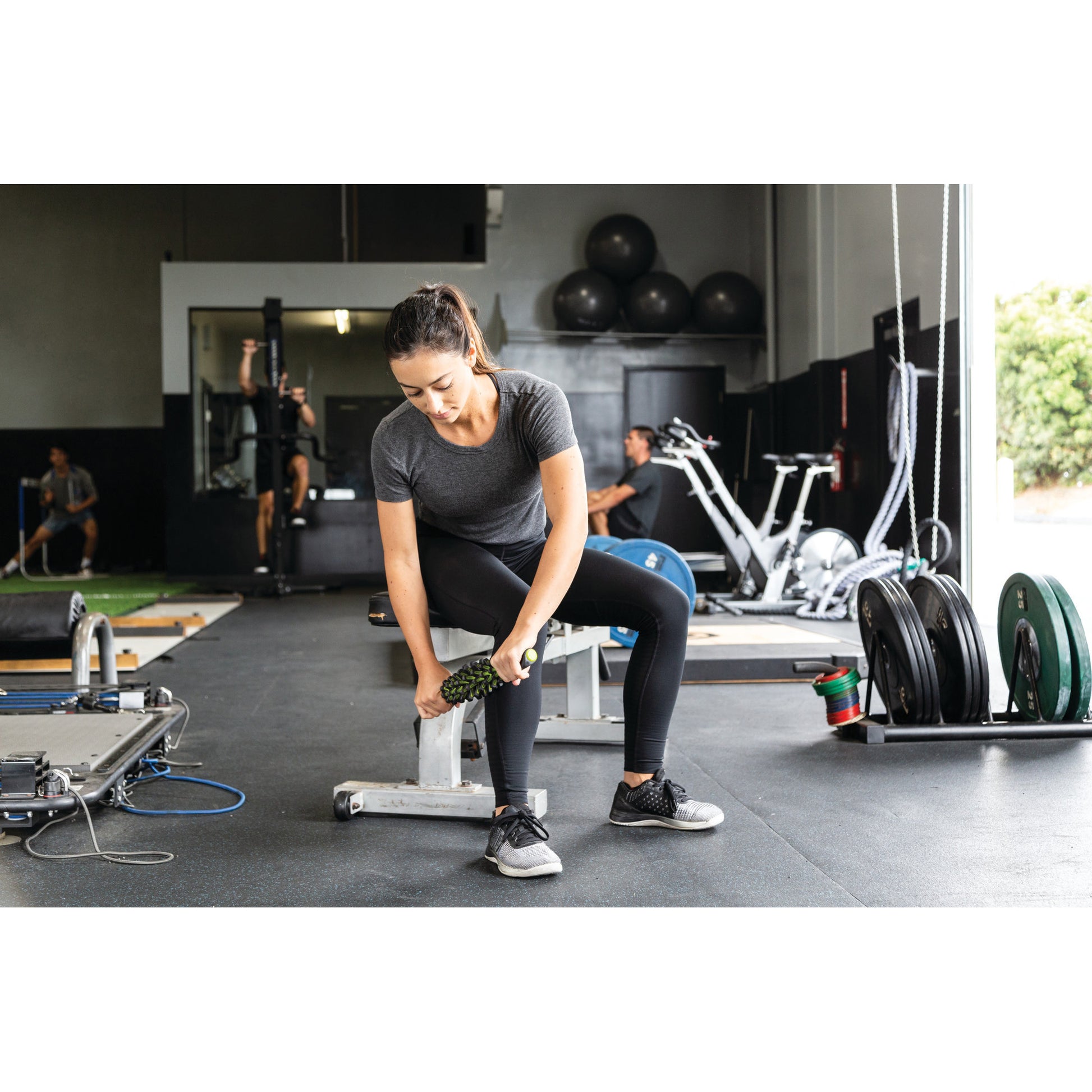 Woman exercises with a dumbbell on a gym floor surrounded by fitness equipment.