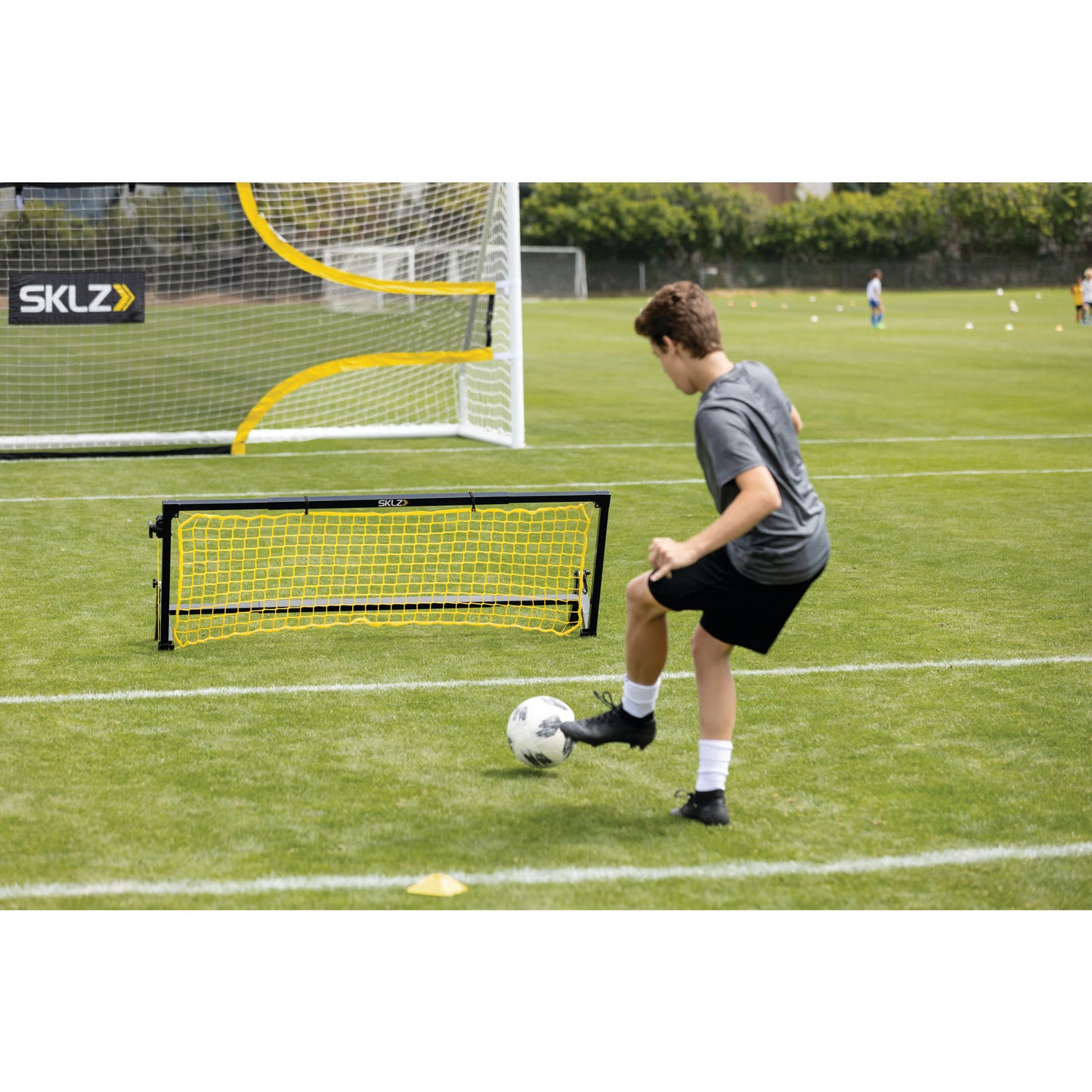 A boy practicing soccer skills kicks a ball near a small goal on a grass field during training.