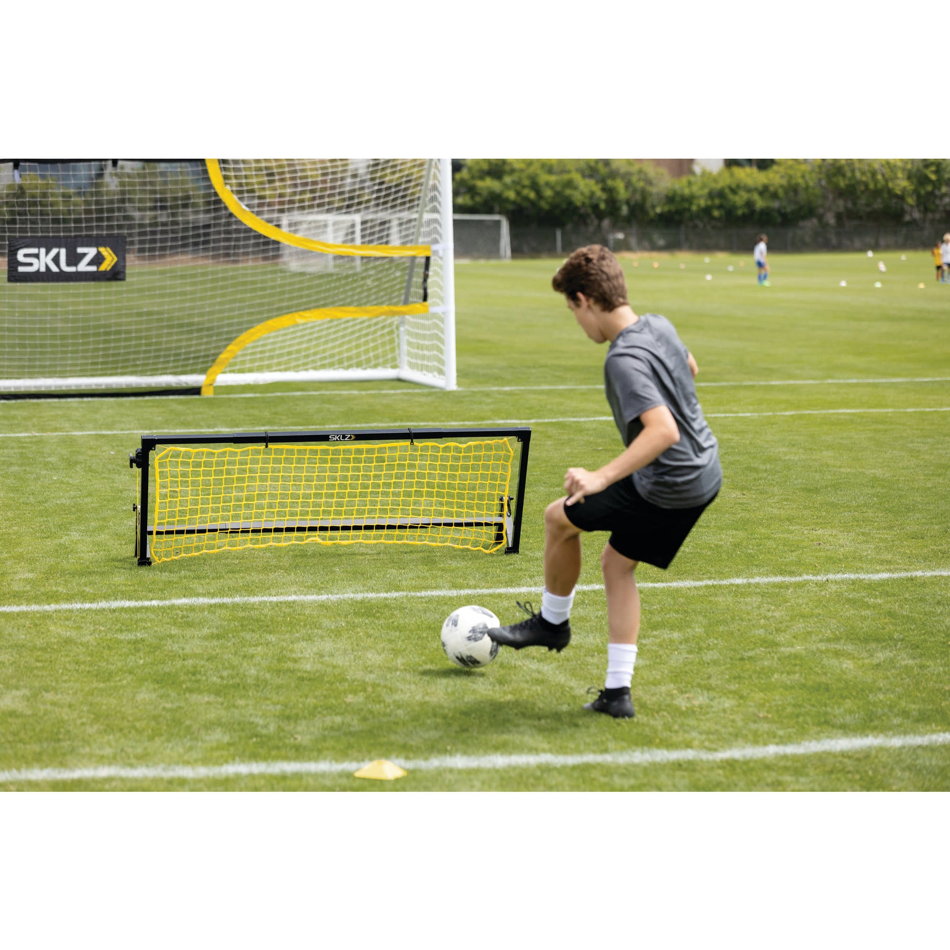 A boy practicing soccer skills kicks a ball near a small goal on a grass field during training.