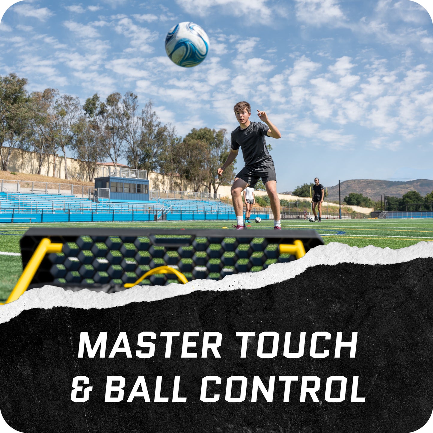 Soccer player strikes ball during practice on field under blue sky with training equipment nearby