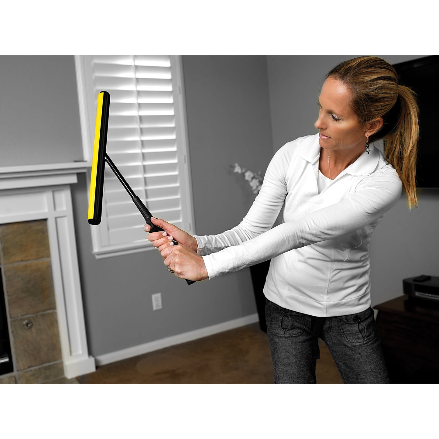 Woman uses a window cleaning tool in a living room with a fireplace and blinds