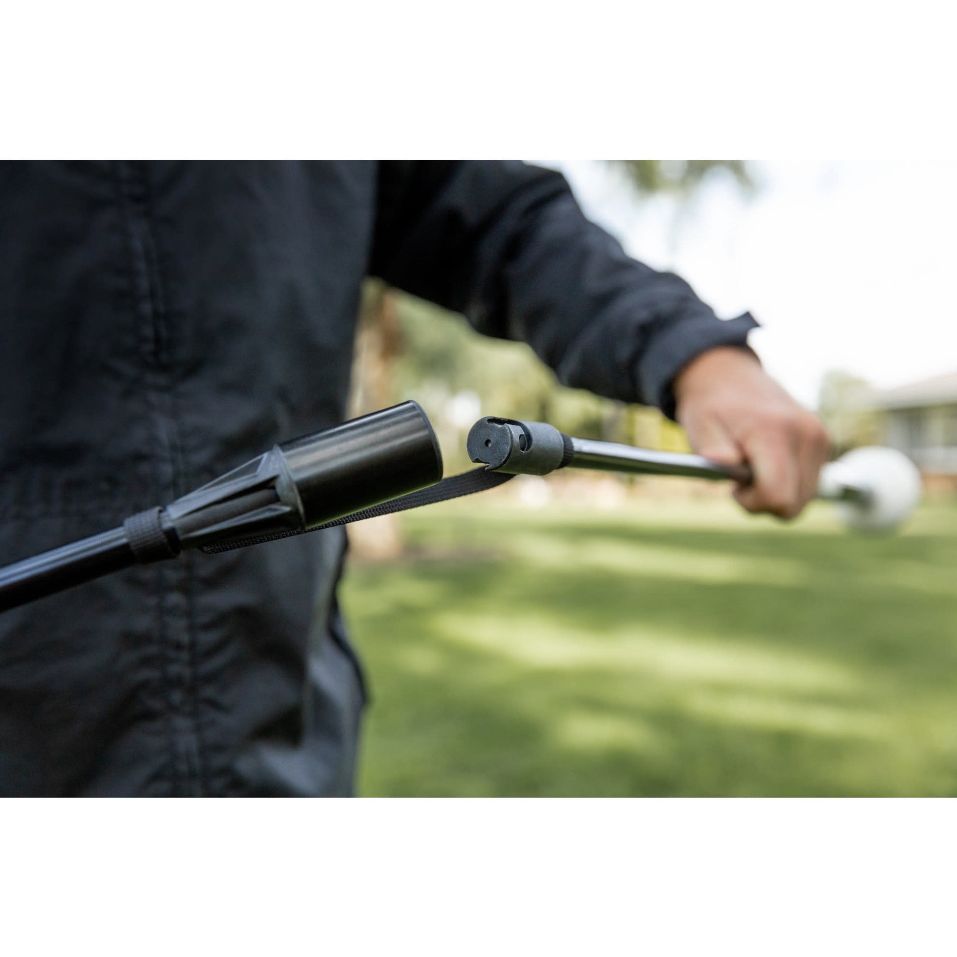 Person holds a long-handled tool outdoors in a grassy area during daytime.