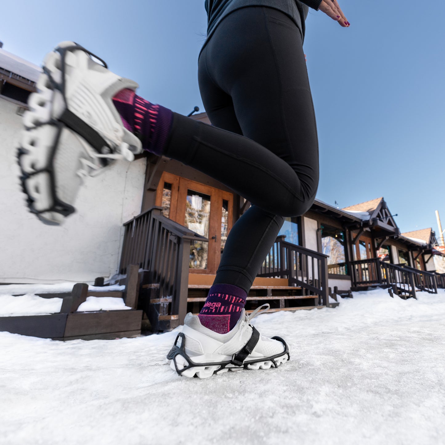 Person runs on snow wearing hiking shoes outdoors in front of wooden cabins