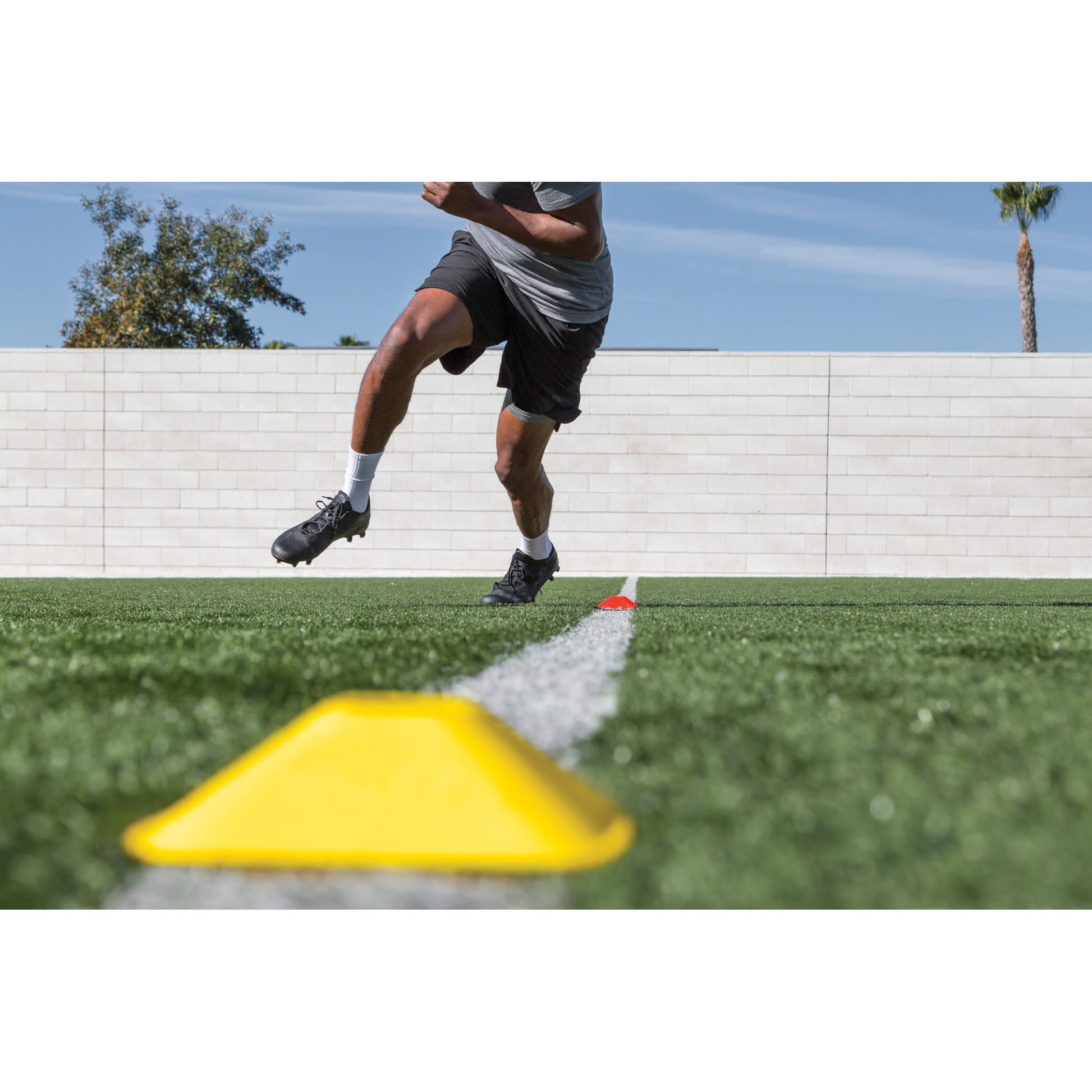 A person runs around a yellow cone on a grassy field during outdoor training