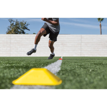 A person runs around a yellow cone on a grassy field during outdoor training