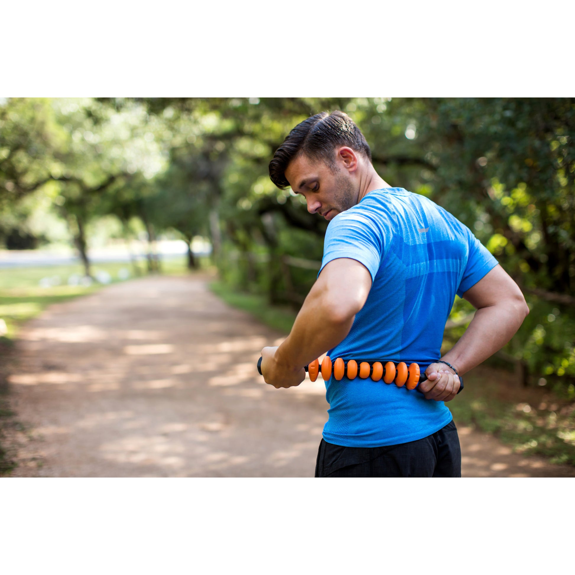 Man stretches his torso with a body roller on a park trail during daytime