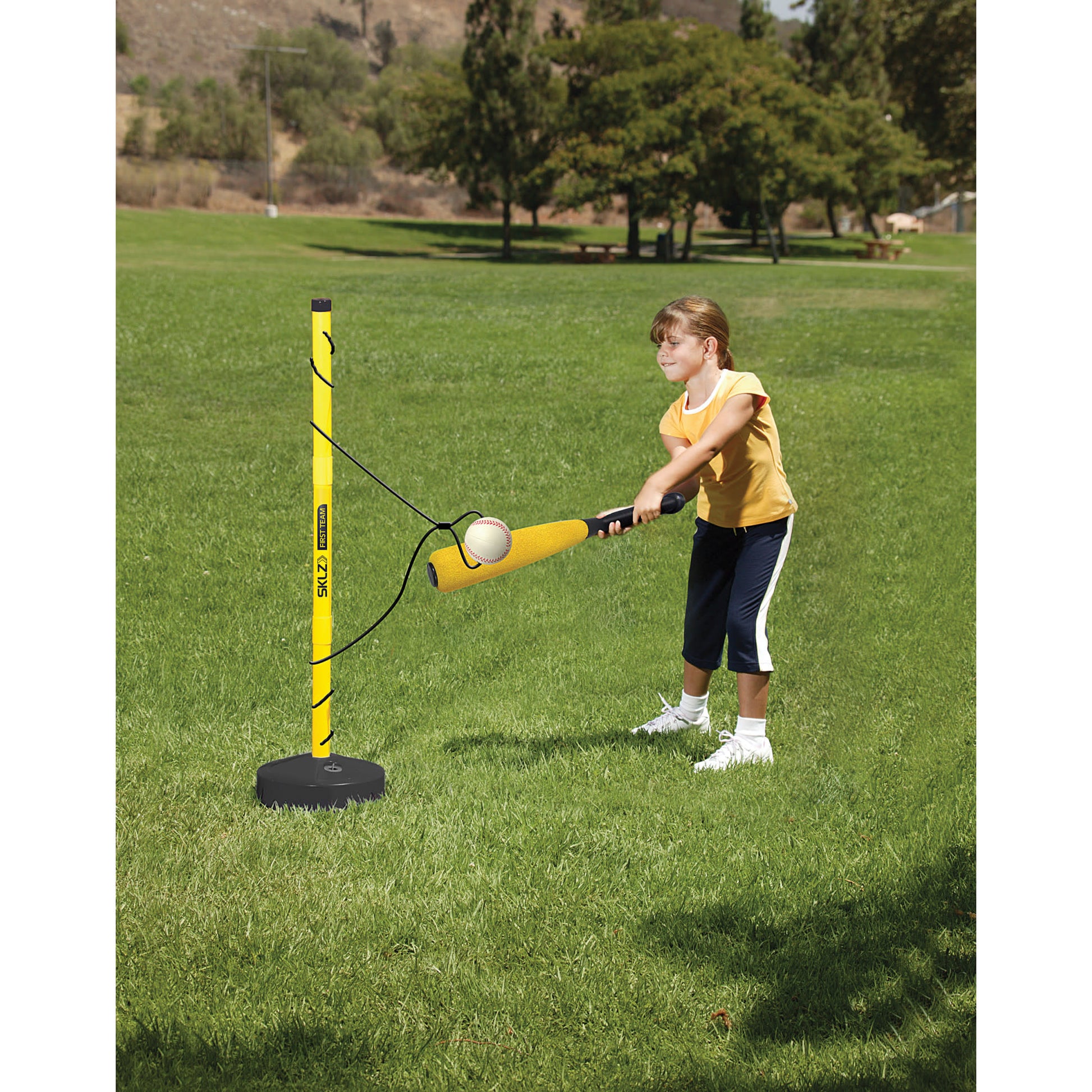 Child swings bat at ball attached to tee on grassy field outdoors