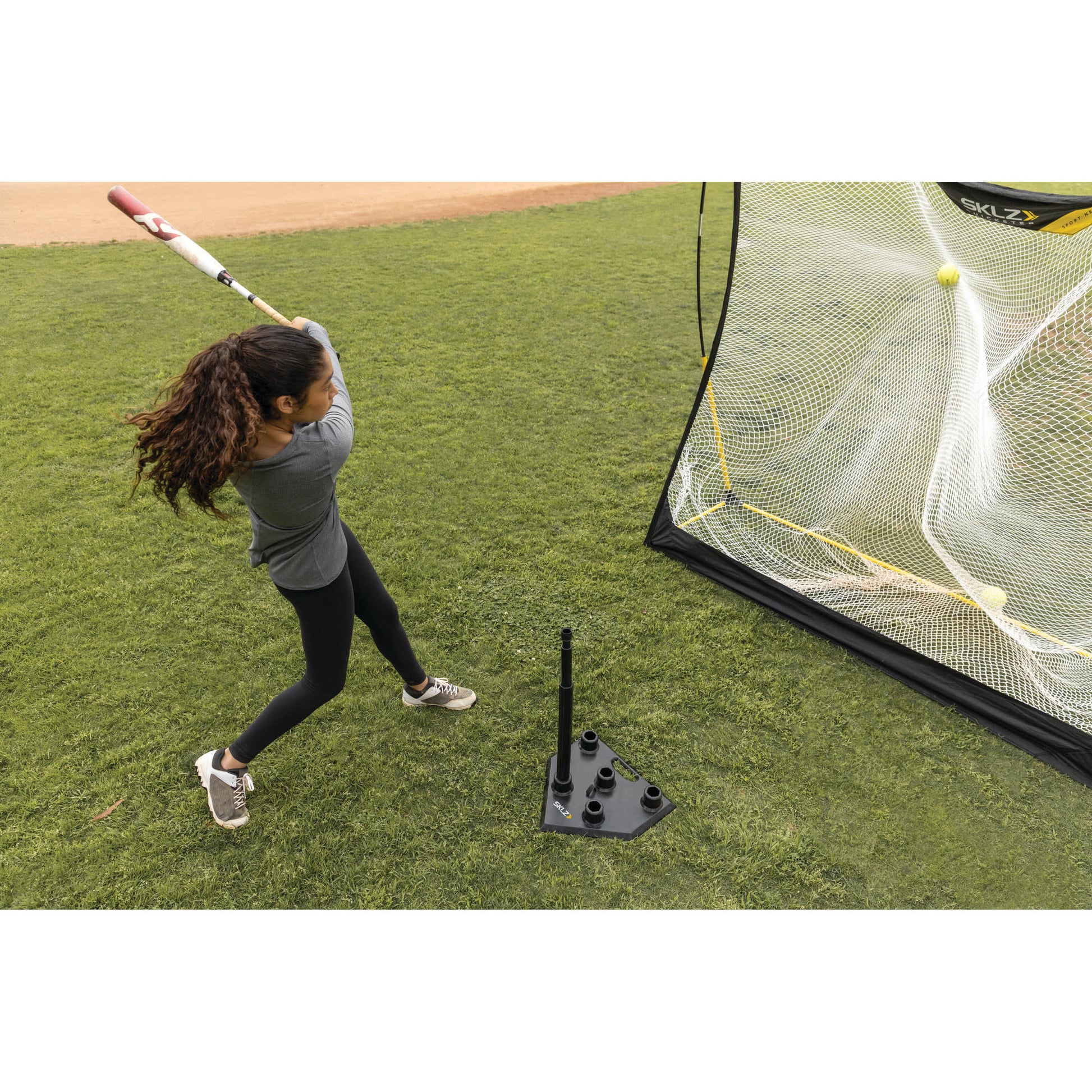 Action shot of a female hitting a ball off the SKLZ 5-position tee on a field into a net