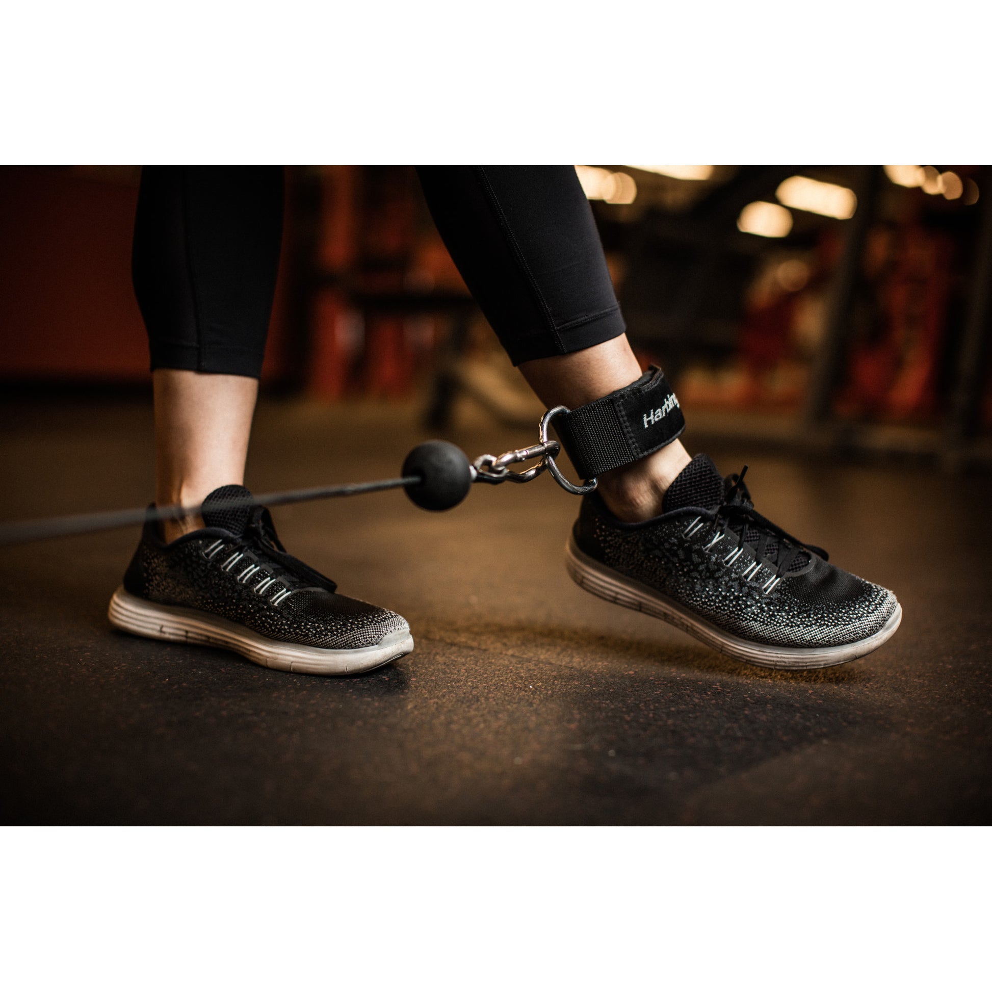 Person exercises with ankle strap weights in a gym environment