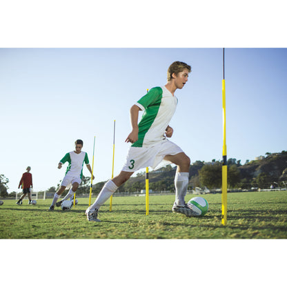 Soccer player dribbles ball through obstacle poles on training field in bright outdoor setting