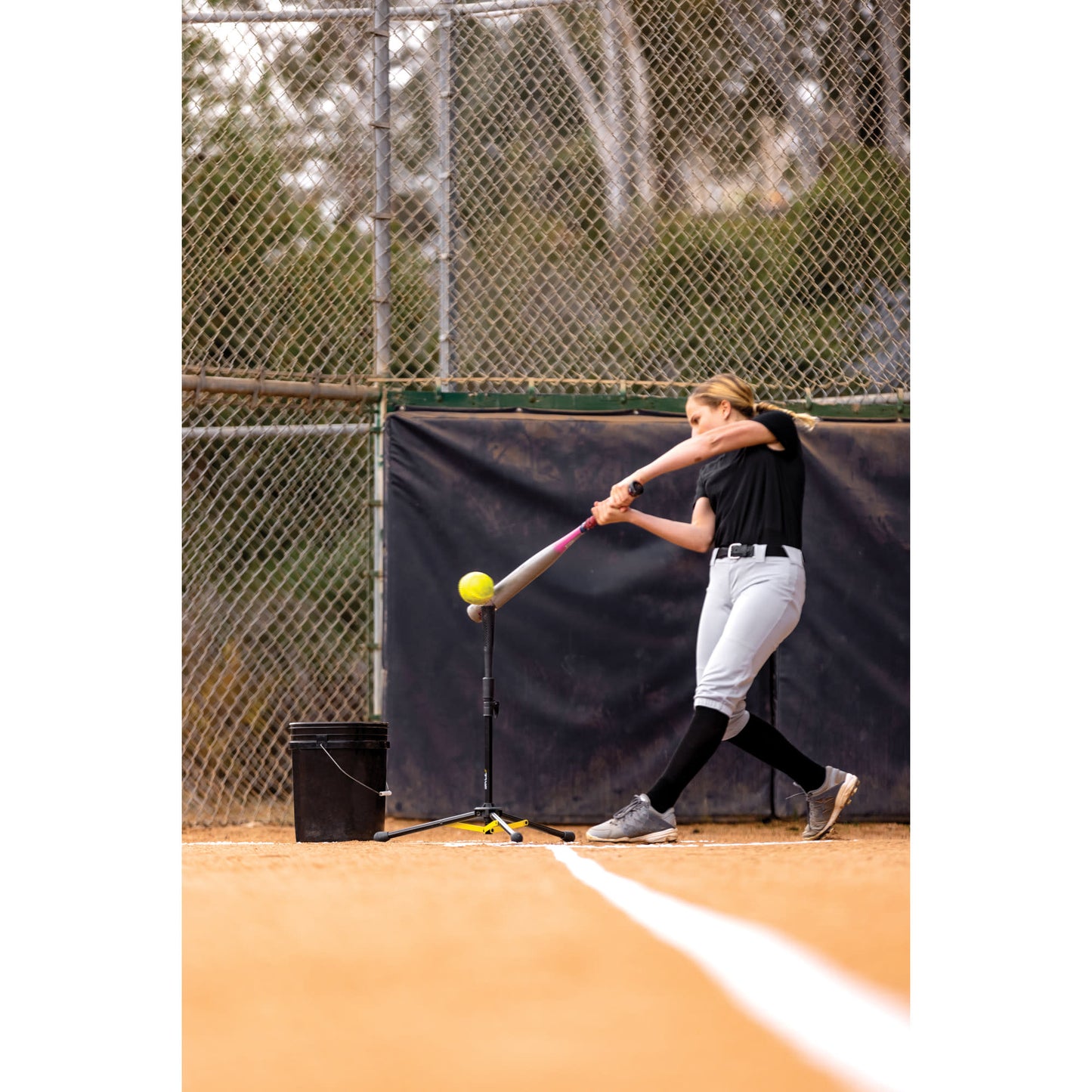 Girl practices batting with a tee on a baseball field during daytime