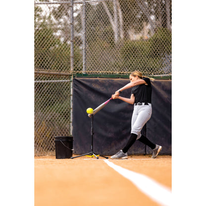 Girl practices batting with a tee on a baseball field during daytime