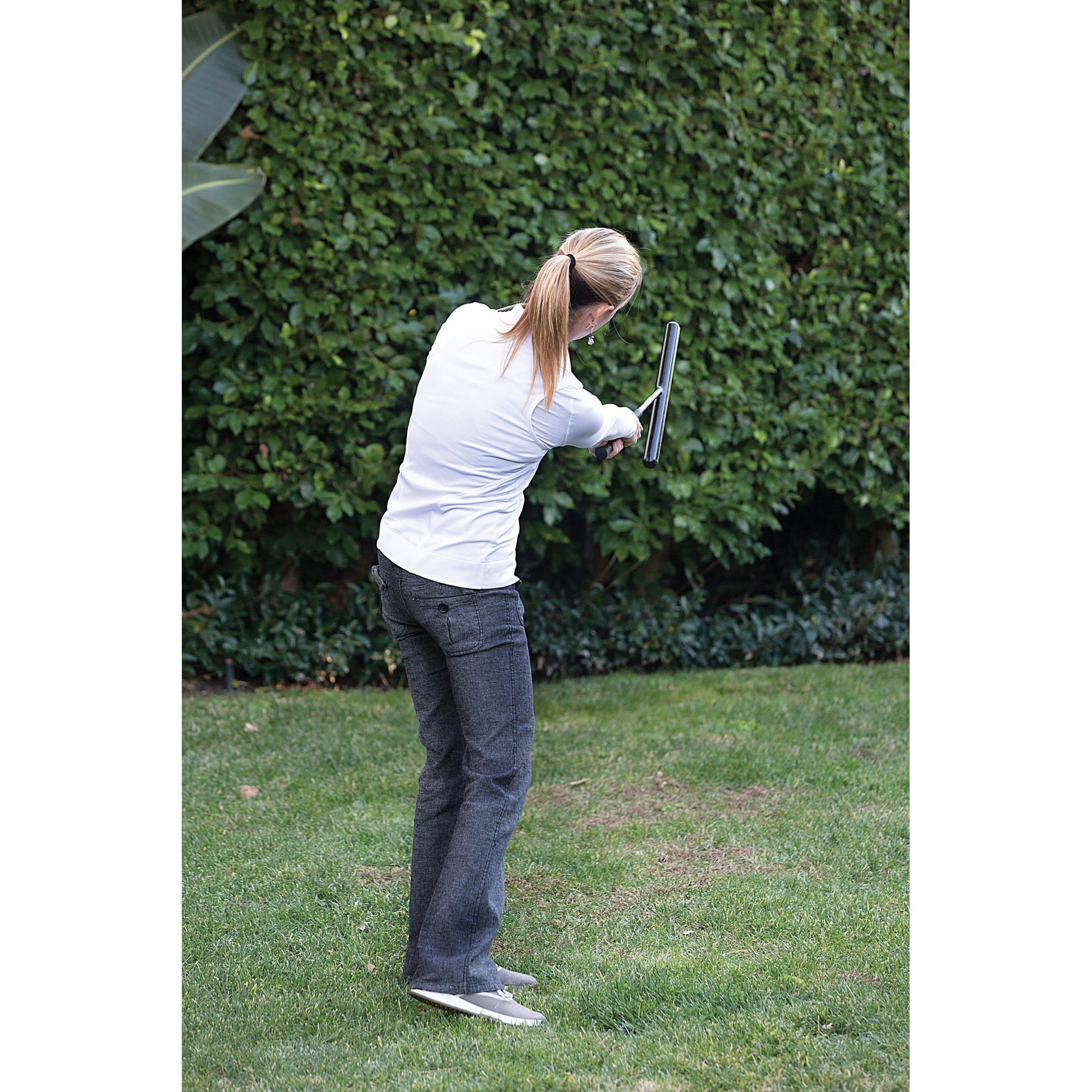 Woman practices golf swing outdoors on grass with green foliage in the background