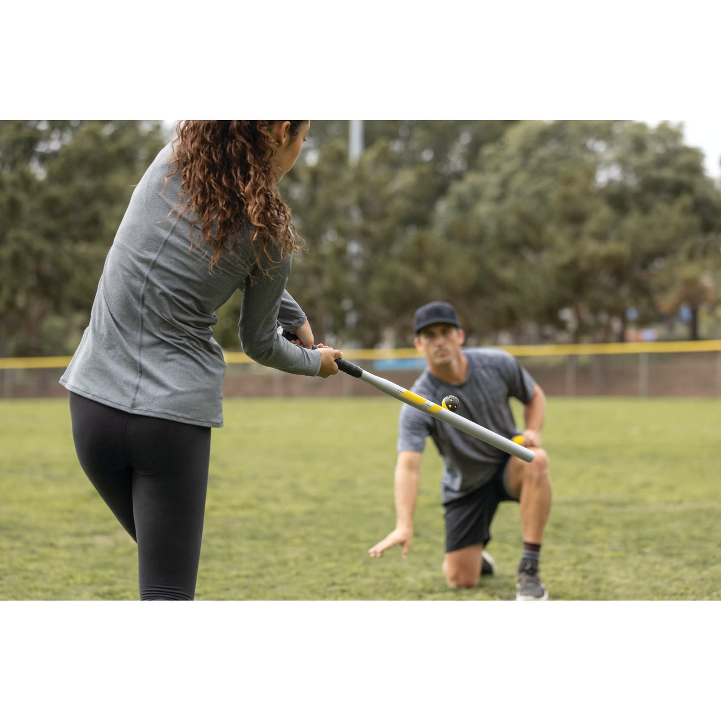 Person swings bat while another person observes on a grassy field during daytime