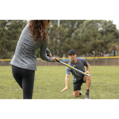 Person swings bat while another person observes on a grassy field during daytime
