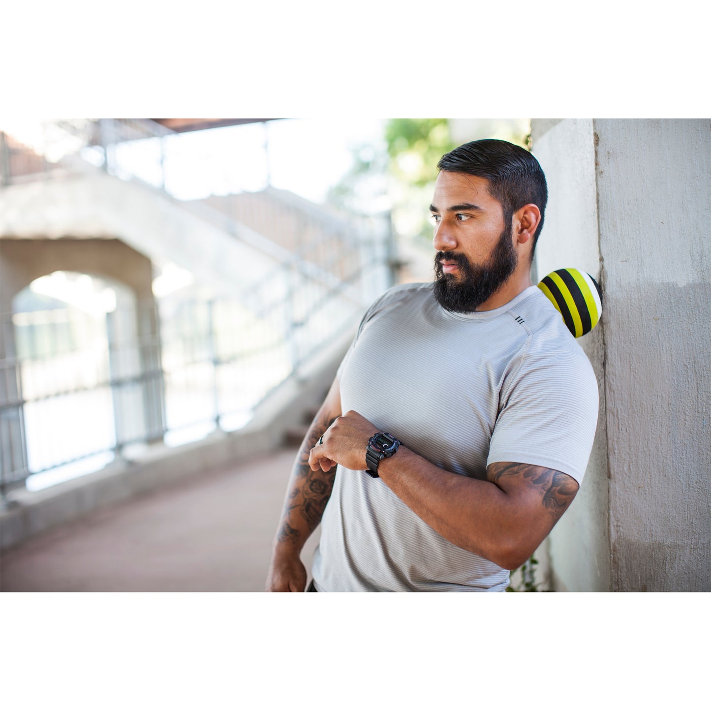 Man leans against wall with a medicine ball behind neck in gym corridor.