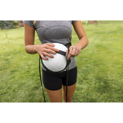 Woman holds volleyball with a strap outdoors on grassy field