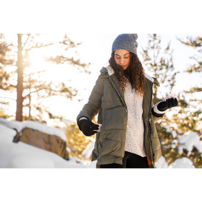 Woman checks her phone outdoors in a snowy forest during winter daytime