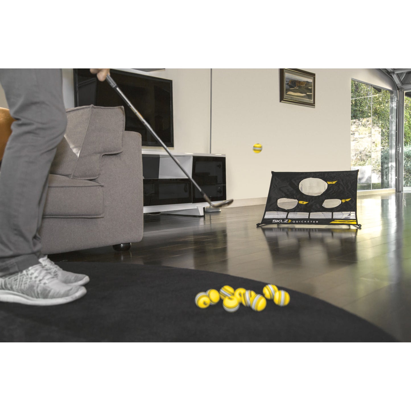 Person practicing golf chip shot indoors using a putter and a training net