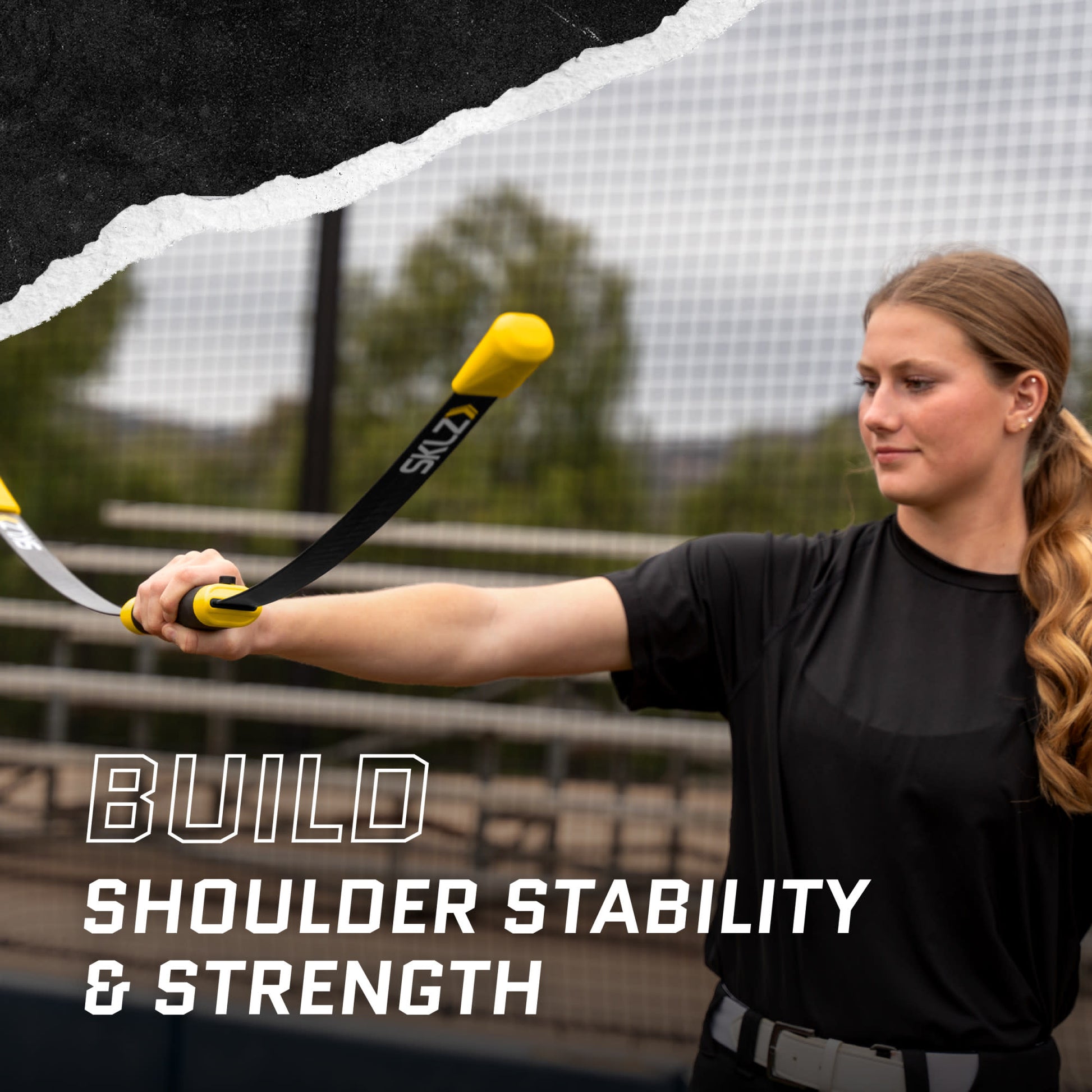Woman holds a resistance band at shoulder level during outdoor training for shoulder stability