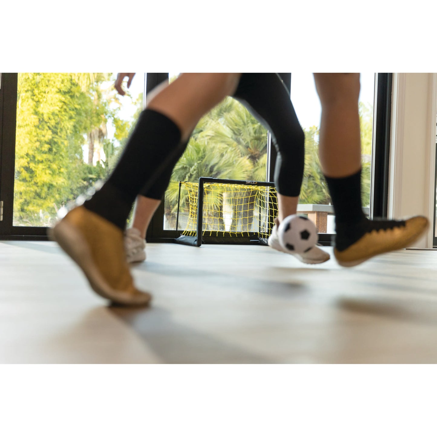 Children kick a soccer ball in an indoor play area with a small goal in the background
