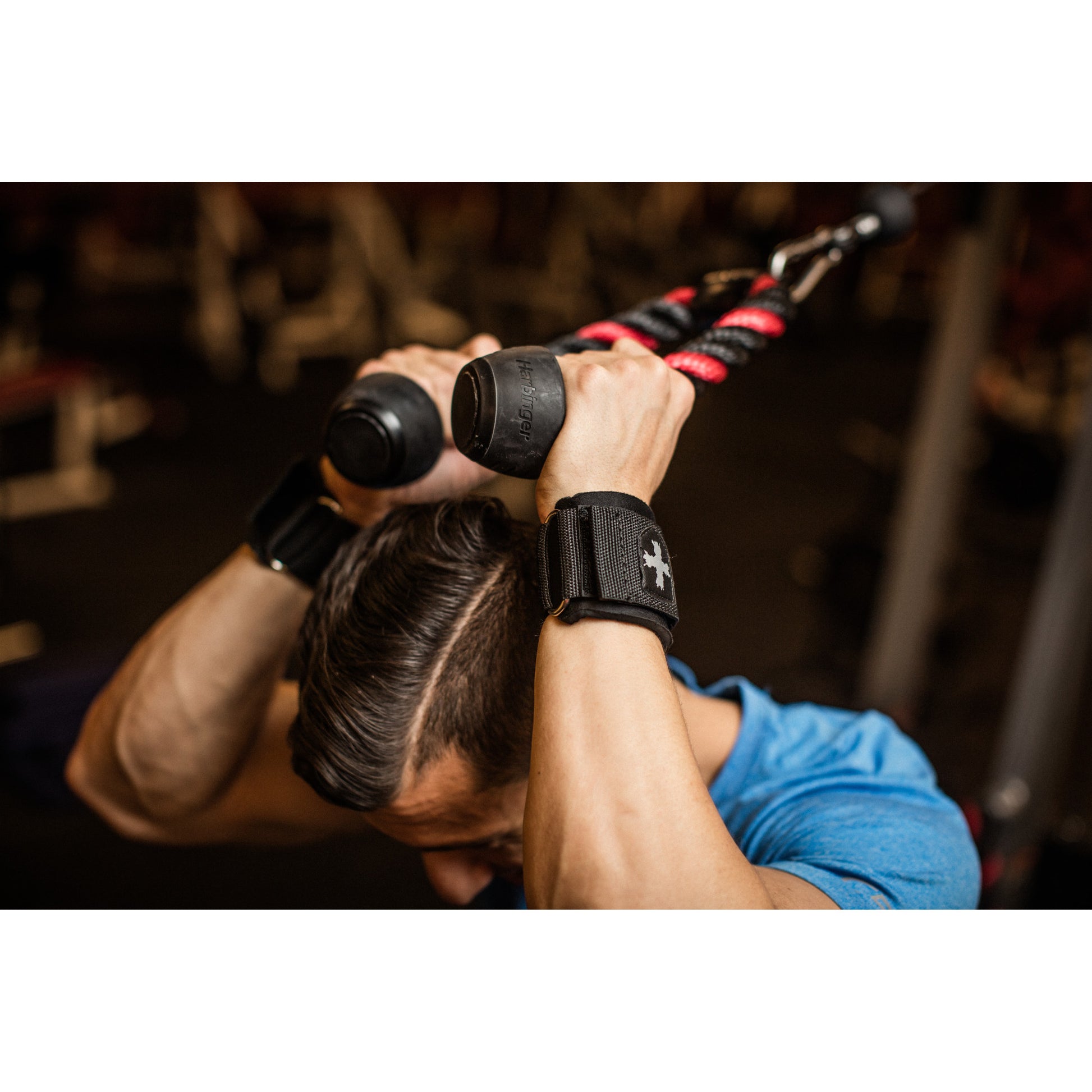 Person exercises using a rope attachment, pulling downward in a gym setting.
