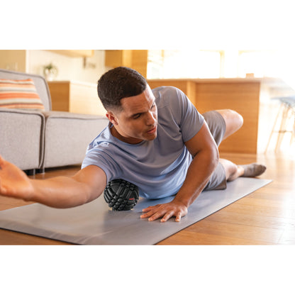 Man exercises with a massage ball on a yoga mat in a living room.