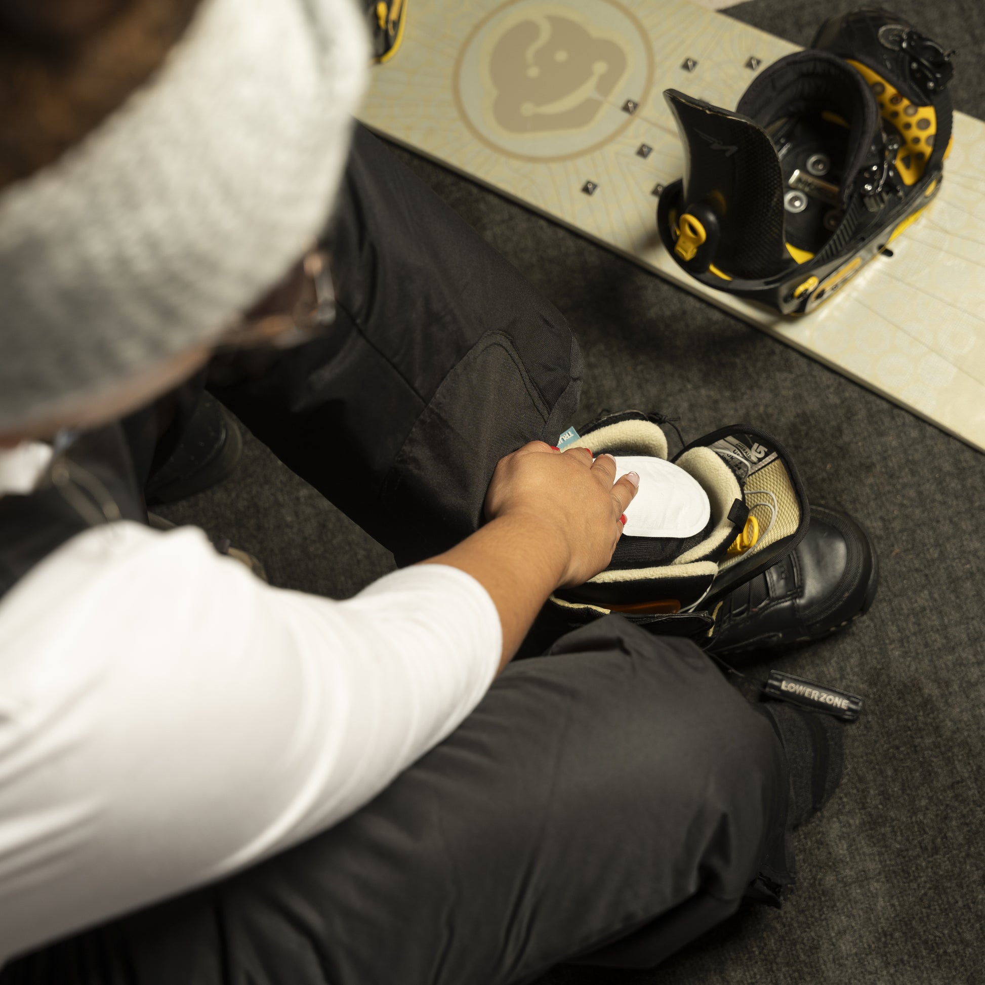 Child puts on a snowboard boot in a skate shop with a skateboard nearby