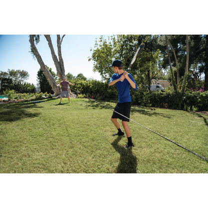 Boy practices golf swing on lawn while another child watches in a garden with trees and bushes