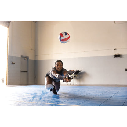 Athlete dives to catch volleyball in an indoor gymnasium with blue tiled floor