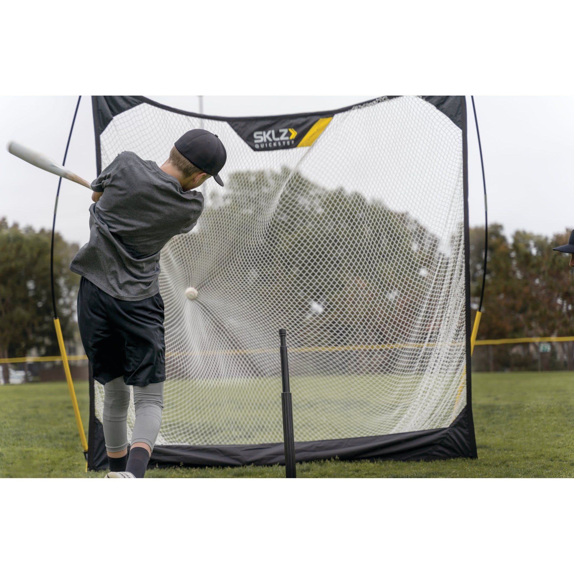 Baseball player practices batting using a pitching net on a grassy field