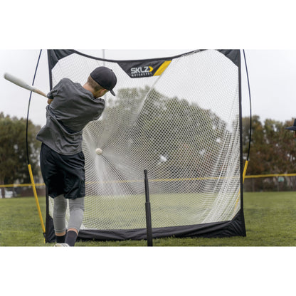 Baseball player practices batting using a pitching net on a grassy field