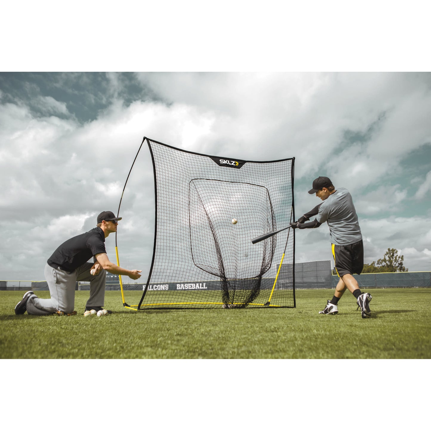 Two boys practice baseball hitting in an outdoor field with a pitching net