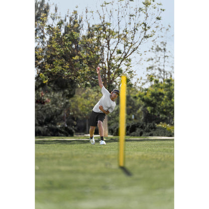 Person bowling in a grassy park with trees in the background.