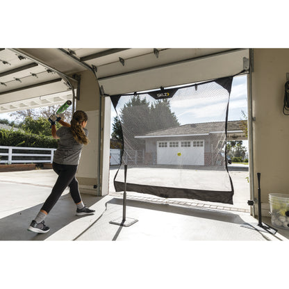 Girl practices baseball swing inside garage using a net for indoor training